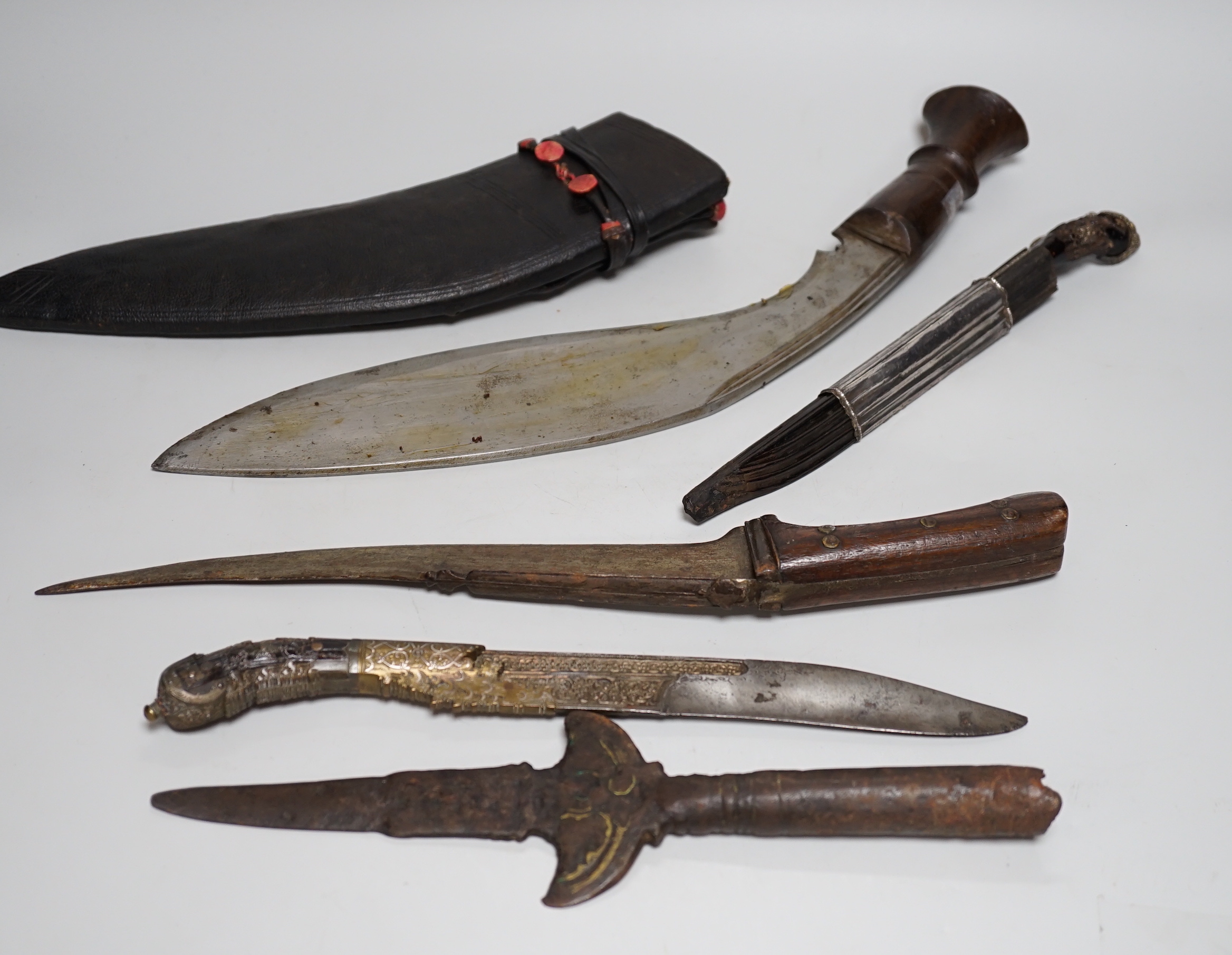 Two Sinhalese daggers and a kukri, a silver inlaid Kirichchiya dagger, together with another in a scabbard with a long pin, another dagger with a wooden handle and a head of a brass inlaid iron pole arm, longest 43cm